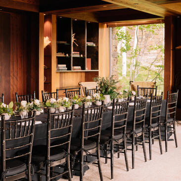 Dining event setup at Amangani with long wooden table, black chairs, and warm wooden interiors overlooking Jackson Hole.