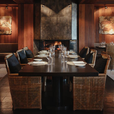 Amangani restaurant dining room with a long black table, woven chairs, and warm amber lighting from wall sconces.
