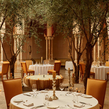 Moroccan restaurant at Amanjena with candlelit table, birch trees and ochre-toned walls.