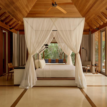 Deluxe pool pavilion at Amanyara with draped four-poster bed and ocean views through open doors.