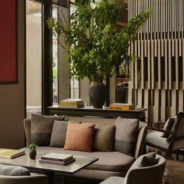 Lounge no Aman New York com sofá cinzento, almofadas coloridas e plantas verdes ao fundo.