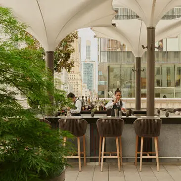 Terraço Arva do Aman New York com bar, plantas e vista para a cidade.