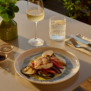 Plated dish with seafood and vegetables at Amanyara beach club resort, accompanied by a glass of white wine.