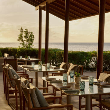Seaside dining venue at Amanyara resort, with tables set beneath a wooden pavilion overlooking turquoise waters.