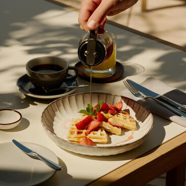 アマンヤラのレストランで、朝食時に紅茶を注ぐ手と、フルーツを添えたエッグベネディクト。