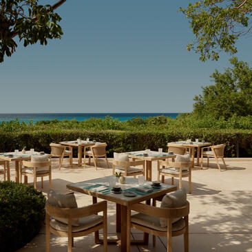 Terrasse de restaurant extérieur d'Amanyara avec tables en bois, vue sur la végétation tropicale et l'océan.