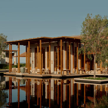 Exterior dining venue at Amanyara resort, featuring wooden architecture reflected in still water at dusk.