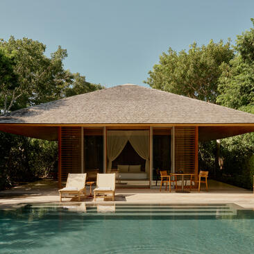 Pool pavilion at Amanyara with thatched roof, wooden lounge chairs and clear blue water.