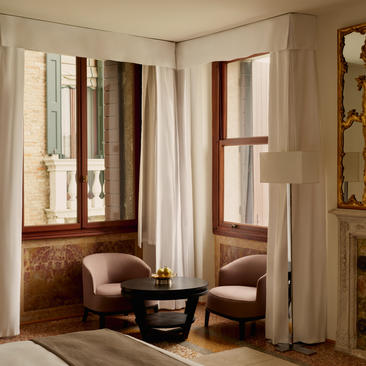 安缦威尼斯酒店大运河宫殿客房，配有落地窗、米色窗帘和两把棕色扶手椅。