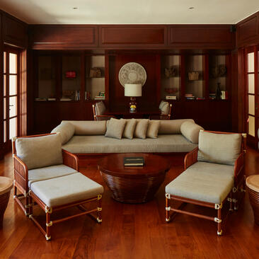 Library at Aman Villas at Nusa Dua with warm wood panelling, built-in shelving and cream seating.