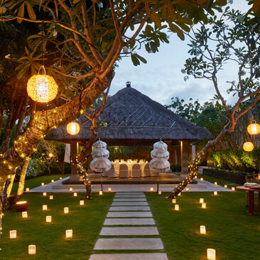 Villa courtyard at dusk with illuminated lanterns lining a pathway towards a traditional structure at Aman Villas at Nusa Dua.
