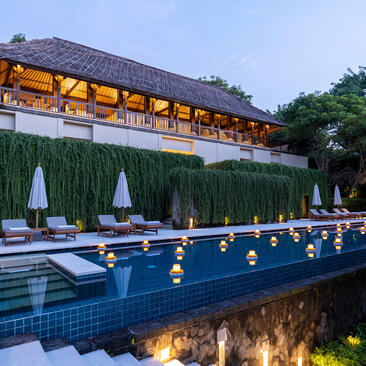Villa 3 pool at Aman Villas at Nusa Dua, illuminated at dusk with loungers and cypress trees lining the water.