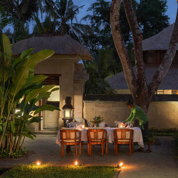 Amandari resort courtyard at dusk with wooden chairs, tropical plants, and candlelit pathways in Ubud, Bali.