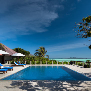 Piscine à débordement avec chaises longues et parasol blanc, baignée de soleil tropical à Amanpulo.