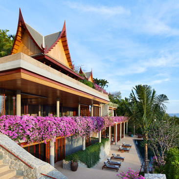 安缦璞瑞度假村的泰式建筑，前方盛开紫红色花朵，绿树环绕。
