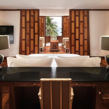 Chambre principale avec lit blanc, bureau en bois sombre et panneaux muraux rouges à Amanpuri.