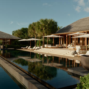 Amanyara villa exterior with wooden deck overlooking a still canal, lush tropical vegetation and clear sky.