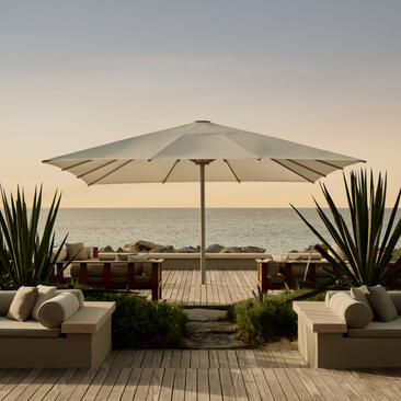 Outdoor terrace at Amanyara with grey umbrella, lounge seating and ocean view at dusk.