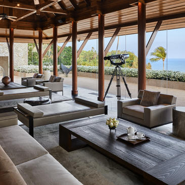 八卧室海滨别墅的宽敞休闲室，配有木质梁架、现代家具和落地窗，俯瞰海景，位于安缦璞瑞度假村。