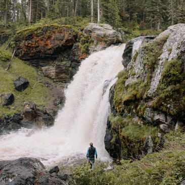 Waterfall cascades through moss-covered rocks at Amangani, Jackson Hole, with a lone figure below.