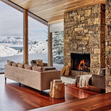 Principal sitting room at Amangani with stone fireplace, wooden floors, and expansive mountain views.