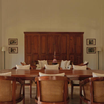 Amantaka's meetings room features dark wood panelling, a long table with rattan chairs, and framed artwork on neutral walls.