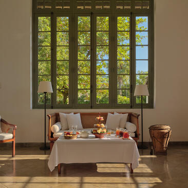 Afternoon tea service laid out on a table in Amantaka's library, with large windows overlooking greenery beyond.