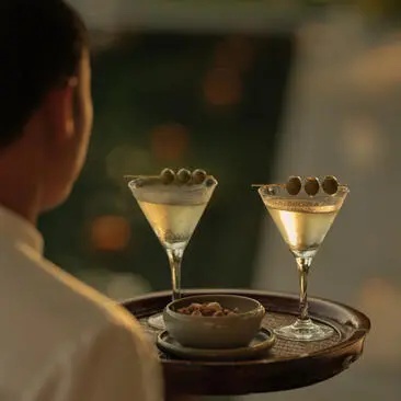 Dirty martinis served at Amantaka's cocktail bar, viewed from behind a guest in soft evening light.