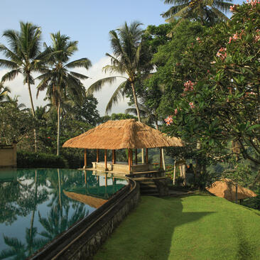Thatched pavilion beside a reflecting pool at Amandari, Bali resort, surrounded by lush gardens and palm trees.