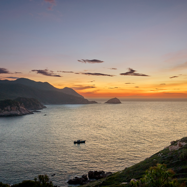 Aerial view of Amanoi resort at sunset, with golden light reflecting across calm waters and forested coastline.