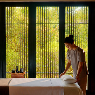 Therapist preparing treatment room at Amanoi spa, with illuminated green-slatted screens behind marble plunge pool.