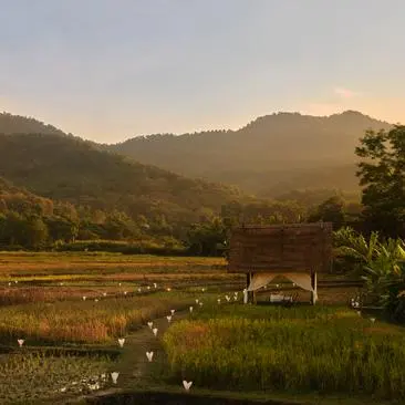 Candlelit dining setup at Amantaka overlooking rice paddies and forested mountains at dusk.