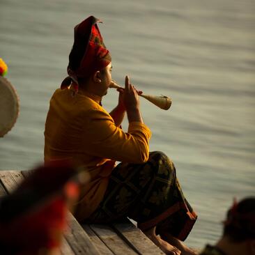 A musician plays a traditional wind instrument whilst seated in a boat at Amanwana, Indonesia, during celebrations.