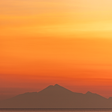 Sunset over volcanic peaks at Amanwana, Indonesia, with warm orange and amber light filling the sky.