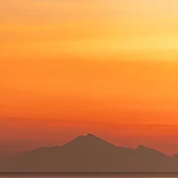 Sunset over volcanic peaks at Amanwana, Indonesia, with warm orange and amber light filling the sky.