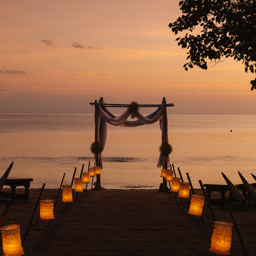 Beachside wedding ceremony at sunset with candle-lit aisle at Amanwana, Indonesia.