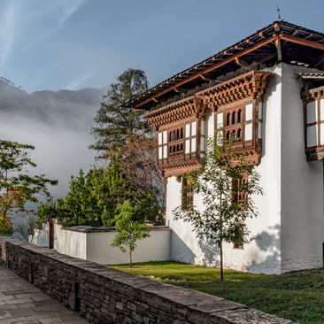 Amankora farmhouse in Punakha with whitewashed walls and traditional wooden details, set amongst mist-covered mountains.
