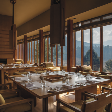 Gangtey dining room at Amankora with wooden table set for service, large windows framing mountain views at dusk.