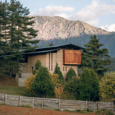 Amankora pavilion with timber cladding set against dramatic Bhutanese mountain peaks, surrounded by evergreen trees.