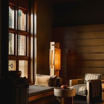 Gangtey Lodge suite interior at Amankora, with wooden window seat overlooking mountain views and warm amber lighting.