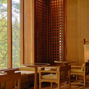 Amankora Thimphu lodge living room with wooden furniture and latticed screen beside tall windows.