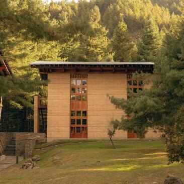 Amankora Paro exterior with terracotta building amongst forested hillside, Bhutan.