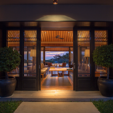Four-bedroom residence entrance at Amanoi, Vietnam, with illuminated wooden doors opening to an interior view at dusk.