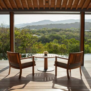 Mountain pool villa terrace at Amanoi with panoramic views over verdant Vietnamese landscape, two leather chairs and side table.