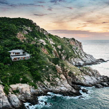 Aerial view of a one-bedroom ocean pool residence at Amanoi perched on a clifftop overlooking Vietnam's coastline at dusk.