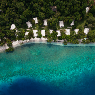 Aerial view of Amanwana's beachfront accommodation pavilions arranged along a turquoise shoreline in Indonesia.