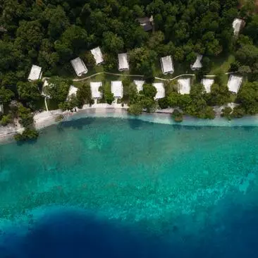 Aerial view of Amanwana's beachfront accommodation pavilions arranged along a turquoise shoreline in Indonesia.