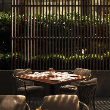 Sala da pranzo dell'Aman New York con tavolo in legno e sedie, illuminata da luce naturale filtrata da persiane in metallo.