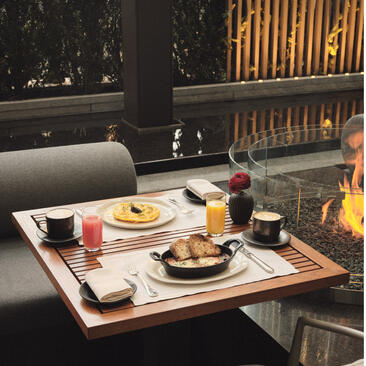 Brunch table at Aman New York with plated dishes, fresh juices, and city views through geometric windows.