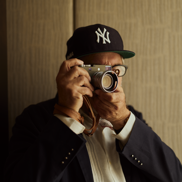 Mark de Paola wearing a New York Yankees cap and glasses against a textured beige wall at Aman New York.